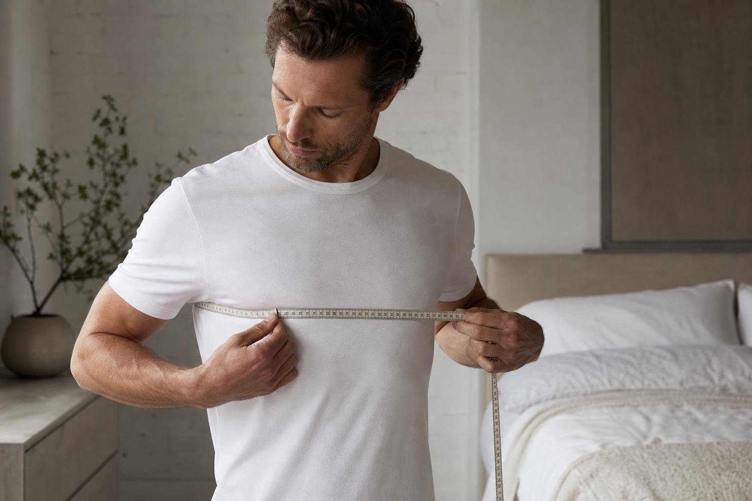 A man measuring his chest with a tape measure for a size guide for men
