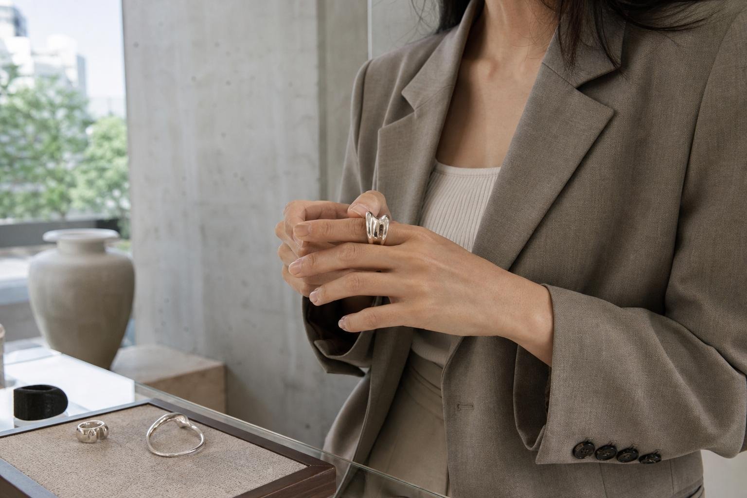Person trying on a sculptural silver ring beside a jewelry counter in soft daylight